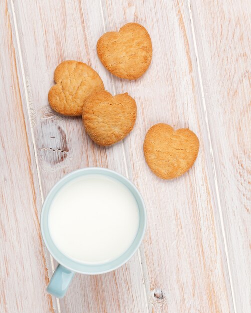 Kopje melk en hartvormige koekjes op witte houten tafel