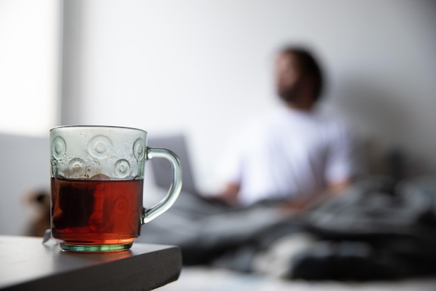 kopje met thee op een tafel, op de achtergrond verschijnt een man onscherp op zijn computer te typen