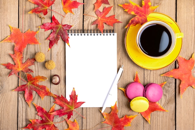 kopje met zwarte koffie, gele lollys, bitterkoekjes, notitieblok, houten tafel met herfst gevallen oranje bladeren plat lag