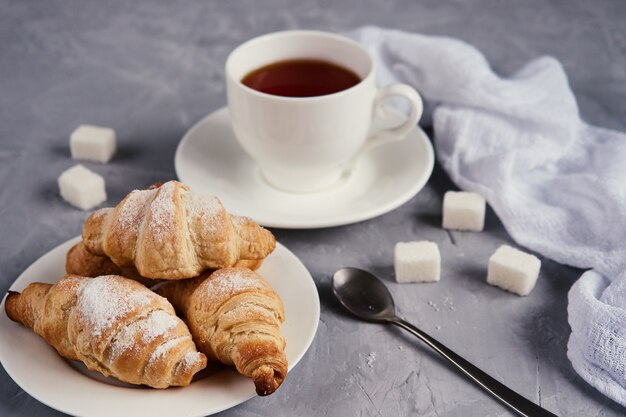 Kopje thee, croissants, suikerklontjes op een grijze achtergrond