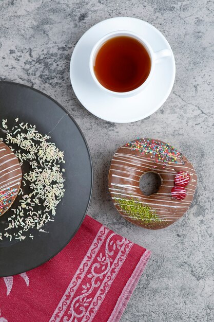 Kopje thee en chocolade donuts met bessen en hagelslag op marmeren oppervlak.