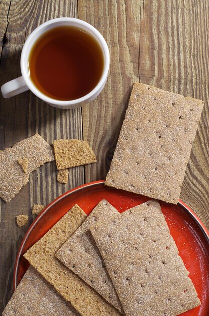 Kopje thee en knapperig brood in rode plaat op de houten tafel, bovenaanzicht. Diëet voeding