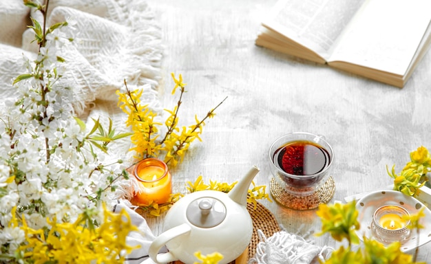 Kopje thee en theepot onder Lentebloemen en brandende kaarsen