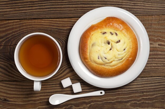 Kopje thee en zoet broodje met kwark en rozijnen voor het ontbijt op houten tafelblad weergave