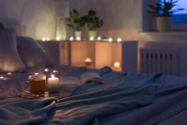Kopje thee met brandende kaars op houten dienblad op bed in de slaapkamer in de avond