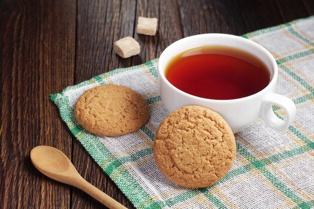 Kopje thee met havermoutkoekje op donker houten tafel bedekt groen tafelkleed