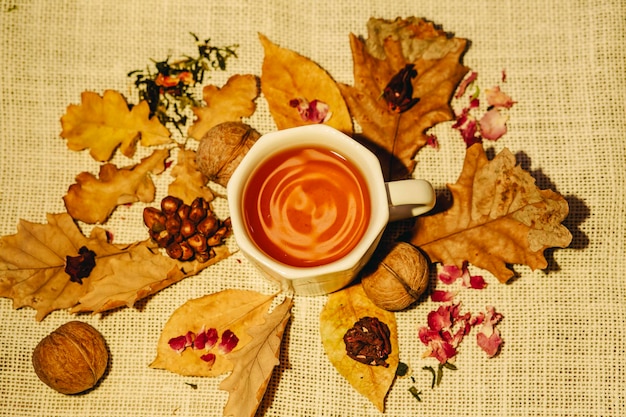 Kopje thee met herfstbladeren, noten en gedroogde theeblaadjes