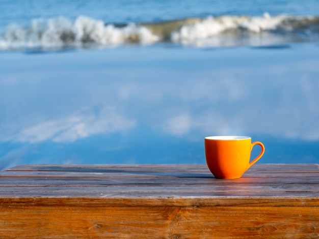 Kopje thee of koffie op houten tafel op het strand, uitzicht op zee