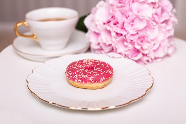 Kopje thee zoete aardbei donut op gouden plaat met hortensia bloem