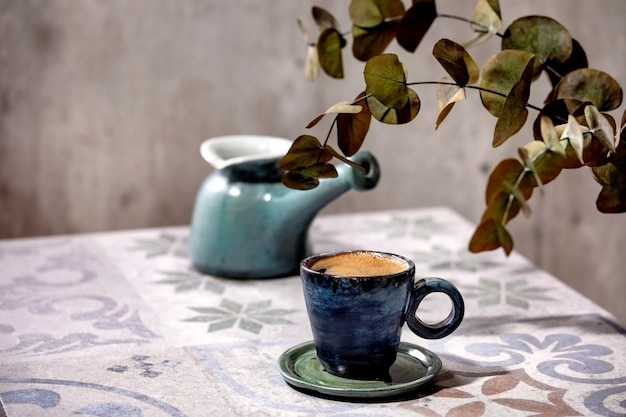 Kopje Turkse zwarte schuimige koffie op sierlijke keramische tafel met koffiepot cezve en eucalyptustakken