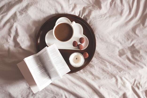 Kopje verse koffie, lychee met open boek en kaars op houten dienblad close-up. Bovenaanzicht. Ontbijt.
