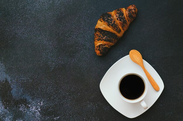 kopje warme koffie en zoete croissant op zwarte achtergrond. Bovenaanzicht, kopieer ruimte, mockup. Plat leggen.