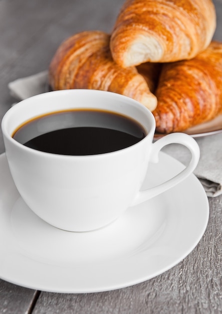 Kopje zwarte koffie en croissant voor ontbijt op houten oppervlak