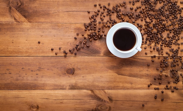 Kopje zwarte ochtendkoffie en koffiebonen verspreid over bruine houten tafel, espresso donkere koffie aroma café winkel achtergrond, warme warme drank drinken in mok, bovenaanzicht, plat lag, close-up kopie ruimte