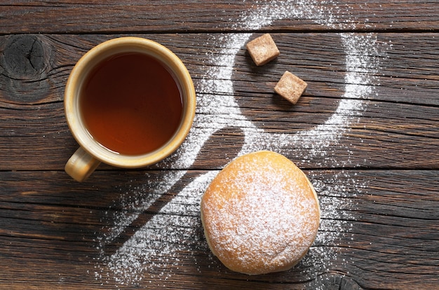 Foto kopje zwarte thee en donut met poedersuiker op het tafelblad-weergave