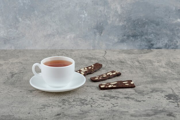 Kopje zwarte thee met cacaocrackers op stenen tafel.