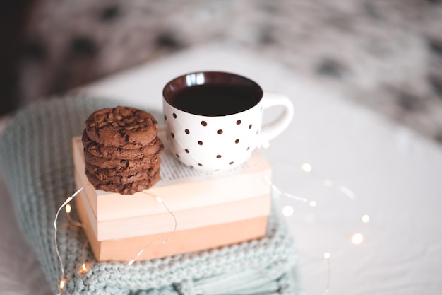 Kopje zwarte thee met chocoladekoekjes die op stapel boeken en gebreide trui close-up in bed blijven. Goedemorgen. Ontbijt. Nachtelijke tijd.