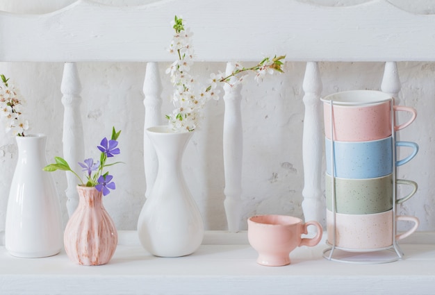 Kopjes en vazen met lentebloemen op vintage houten witte plank