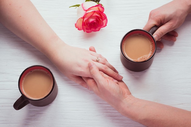 Kopjes koffie, rose en hand in hand van verliefde paar op witte houten tafel. Concept romantische date op Valentijnsdag. Bovenaanzicht, plat gelegd