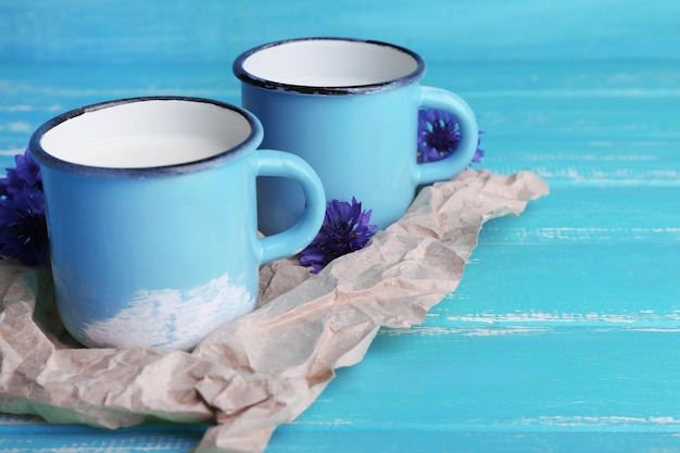 Kopjes melk en korenbloemen op houten tafel