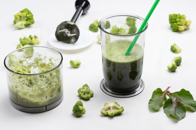 Kopjes met groene groente smoothies Metalen chopper op schotel Takjes rozemarijn en broccoli op tafel