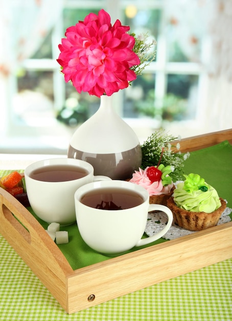 Kopjes thee met bloem en gebak op houten dienblad op tafel in de kamer