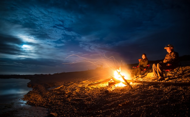 Foto koppel met kampvuur op rotsachtige strand bij nacht