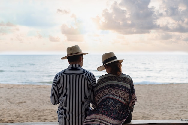 Koppel met strohoed zittend op het strand wanneer de zonsondergang