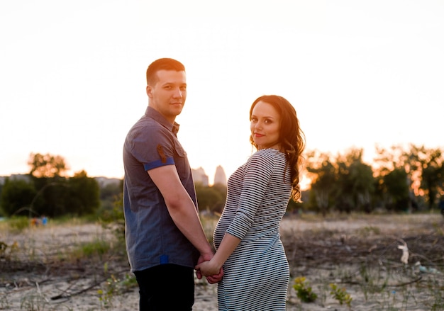 Koppel met zwangere vrouw hand in hand op zonsondergang