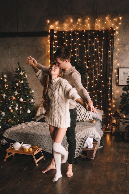 Koppel op het bed in de slaapkamer. Donker interieur. Nieuwjaar en Kerstmis. Knuffels en kussen. Dol zijn op. Witte trui en hoge sokken. Romantische ontmoeting. Liefhebbers van een date.