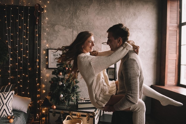 Koppel op het bed in de slaapkamer. donker interieur. nieuwjaar en kerstmis. knuffels en kussen. dol zijn op. witte trui en hoge sokken. romantische ontmoeting. liefhebbers van een date.