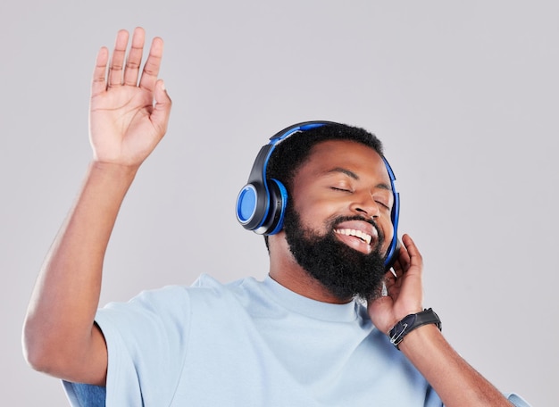 Koptelefoon zingt en man in een studio met muziekafspeellijst of album terwijl hij danst met energie Gelukkige glimlach en jong Afrikaans mannelijk model luisterend naar een liedje of radio online geïsoleerd door grijze achtergrond