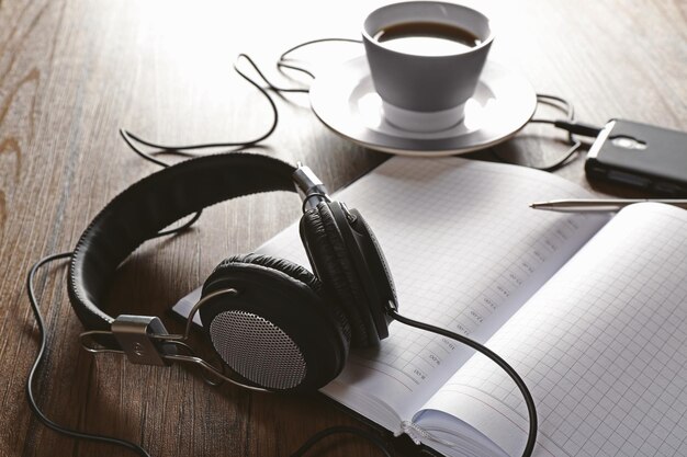 Koptelefoons met papieren en een kop koffie op een houten tafel