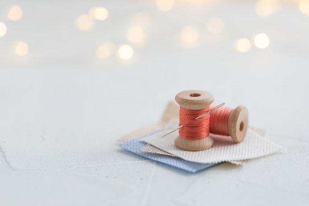 Koraal gekleurde draden houten spoel voor het naaien met een naald op een linnenpak op witte achtergrond