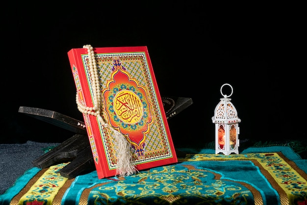 Koran op een houten placemat in gebedskleed met gebedskralen en arabische lamp op donkere achtergrond