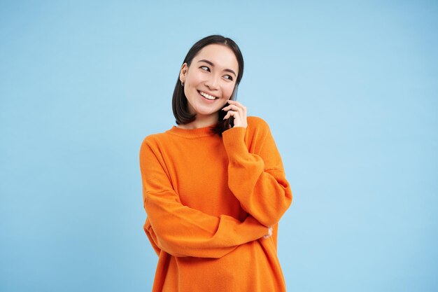 Koreaans meisje in oranje sweater praat op mobiele telefoon en spreekt op mobiele telefoon met blij lachend gezicht