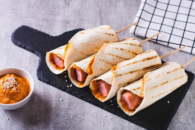 Koreaanse straatvoedsel maïshond in tortilla grill met saus op leisteen op tafel