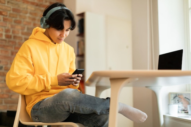 Koreaanse tiener die een mobiele telefoon gebruikt en thuis een koptelefoon draagt