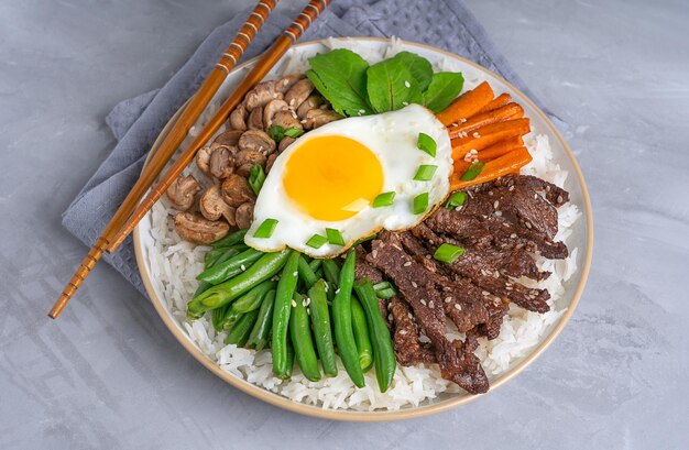 Korean Bibimbap made of boiled rice topped with beef slices green beans mushrooms and fried egg