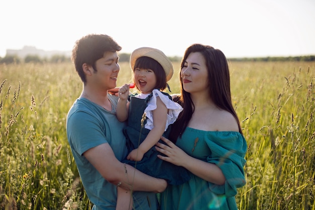 Korean family with their daughter go to the field in the grass at sunset