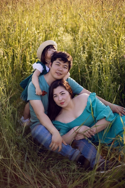 Korean family with their daughter lie in a field in the grass at sunset