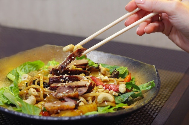 韓国料理。女の子はお箸で肉、ナッツ、野菜の韓国料理を食べます。