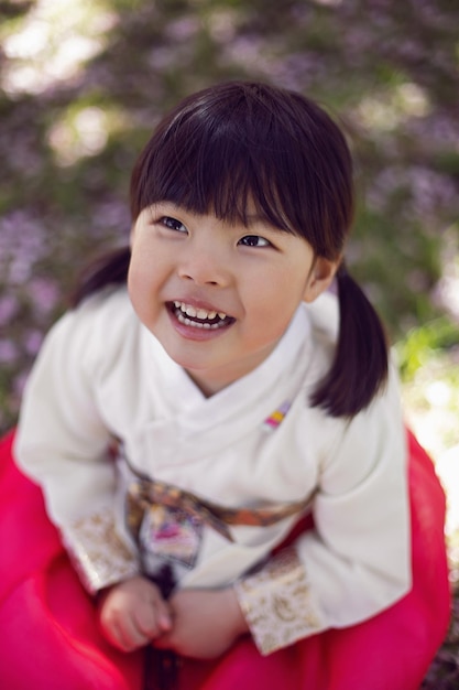 Photo korean girl child in a national costume walks in a garden with cherry blossoms in spring