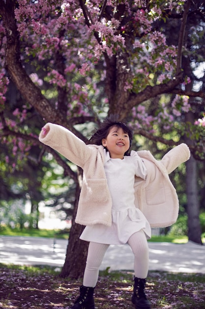 白い毛皮のコートとヘッドバンドの韓国の女の子が桜のある庭を走る