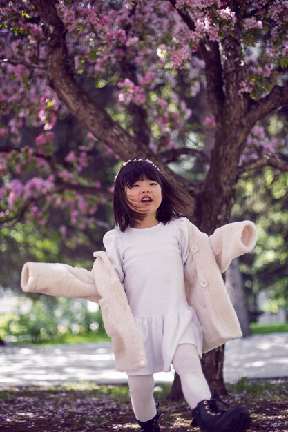 하얀색 모피 코트와 머리띠를 한 한국 소녀가 벚꽃이 만발한 정원에 서 있다
