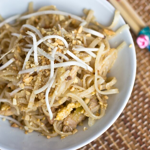 Korean rice noodles with soybean sprouts and crushed peanuts in a white bowl with chopsticks