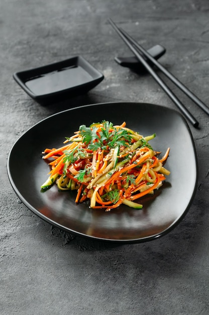 Insalata coreana con patate crude e verdure in una ciotola nera sfondo scuro vista dall'alto