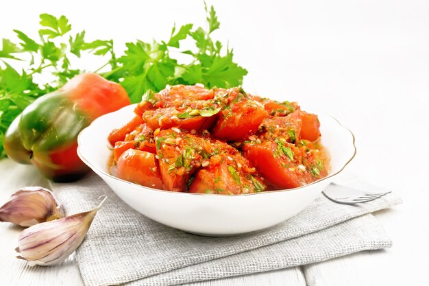 Korean style tomatoes with sweet and hot peppers, garlic and spices in a plate on a towel on wooden board background