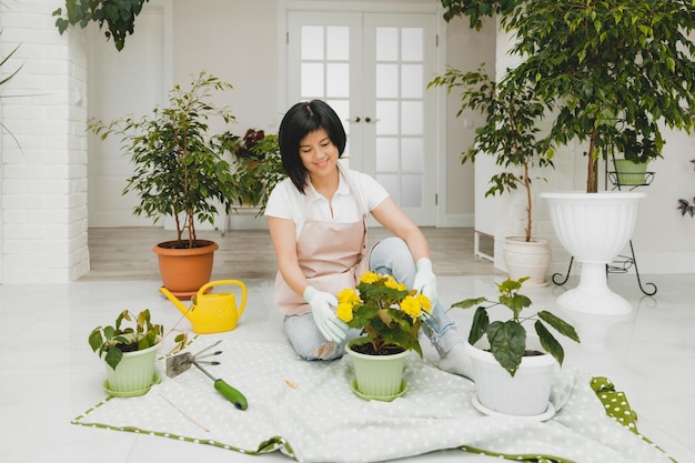 A Korean woman in an apron takes care of plants and flowers in a pot Home gardening and floriculture