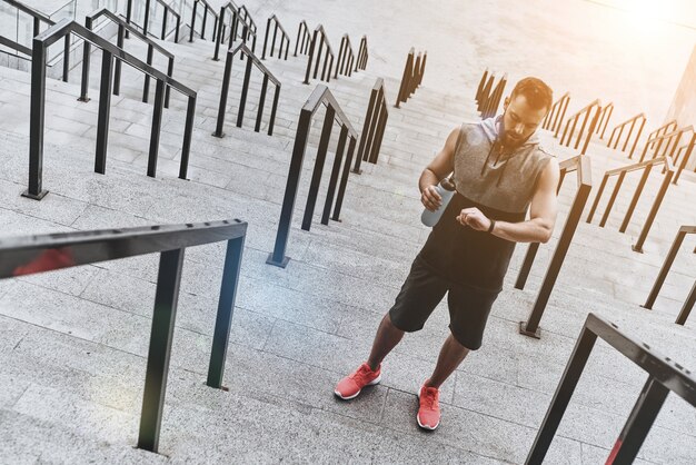 Korte rust hebben. Knappe jongeman in sportkleding die naar zijn fitnesstracker kijkt